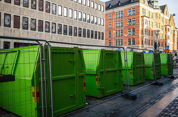 green construction waste containers behind fence on urban street